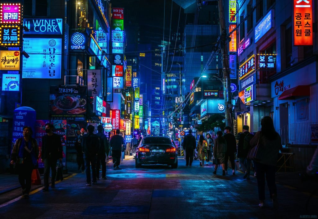 Fotografía Cyberpunk de un callejón colorido en Seúl con la vista trasera de un coche y varias personas a los lados