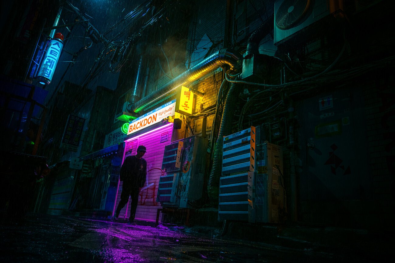 Foto con atmósfera Cyberpunk de un callejón oscuro de Seúl, lloviendo, con luces de colores y una silueta de una persona