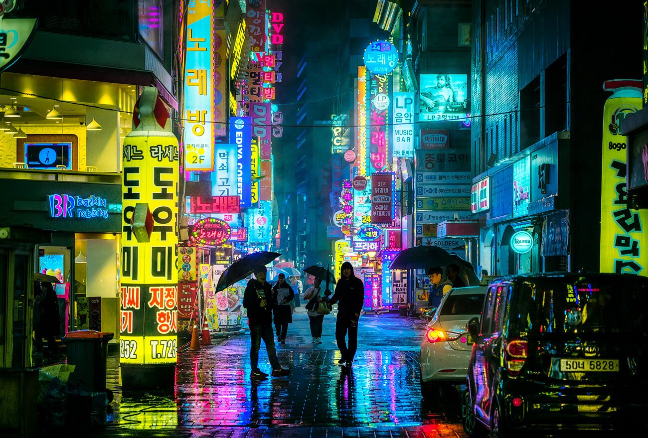 Calle con una explosión de luces de colores con aspecto Cyberpunk, lloviendo y gente con paraguas